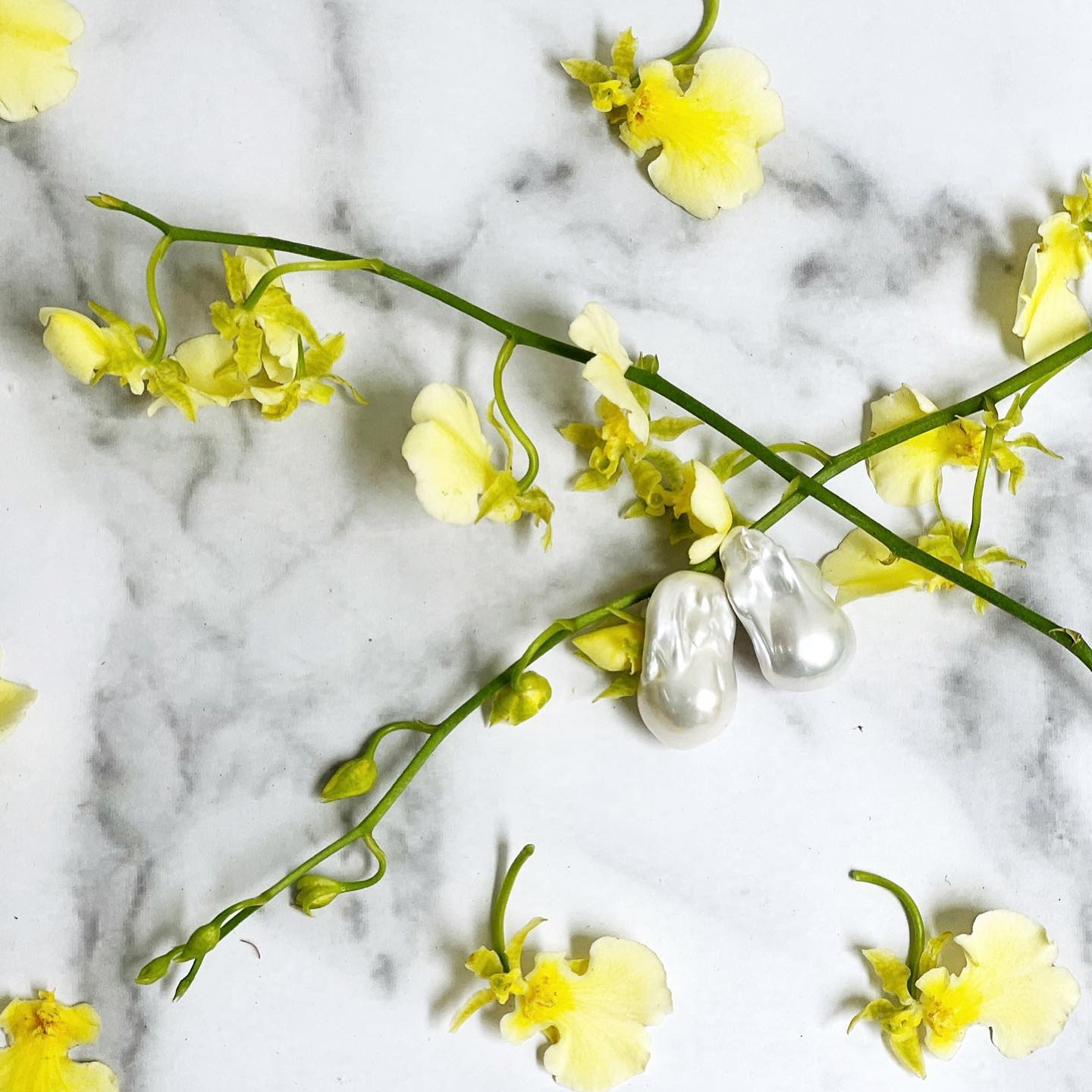 Closeup of Baroque Pearl Stud Earrings on marble background with some yellow flowers