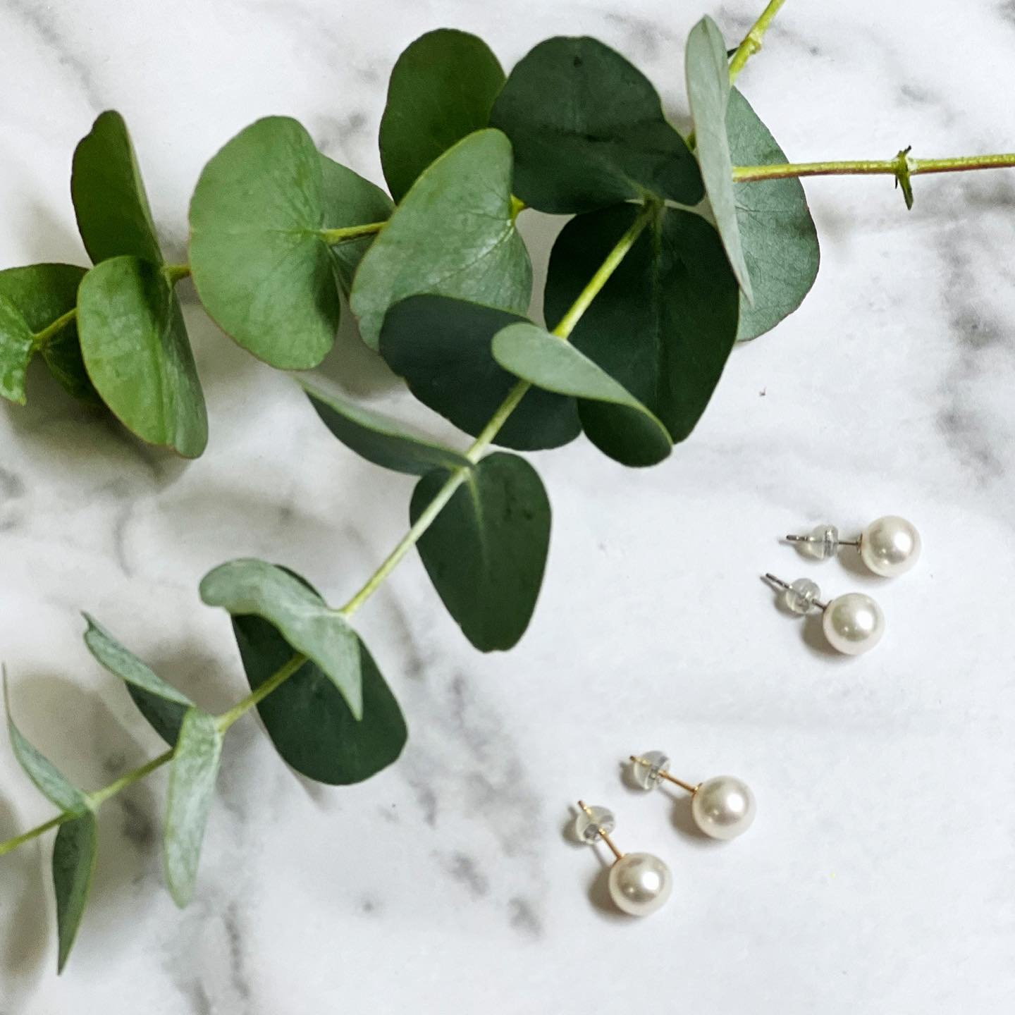 Closeup of Akoya Classic Earrings on marble background with some leaves