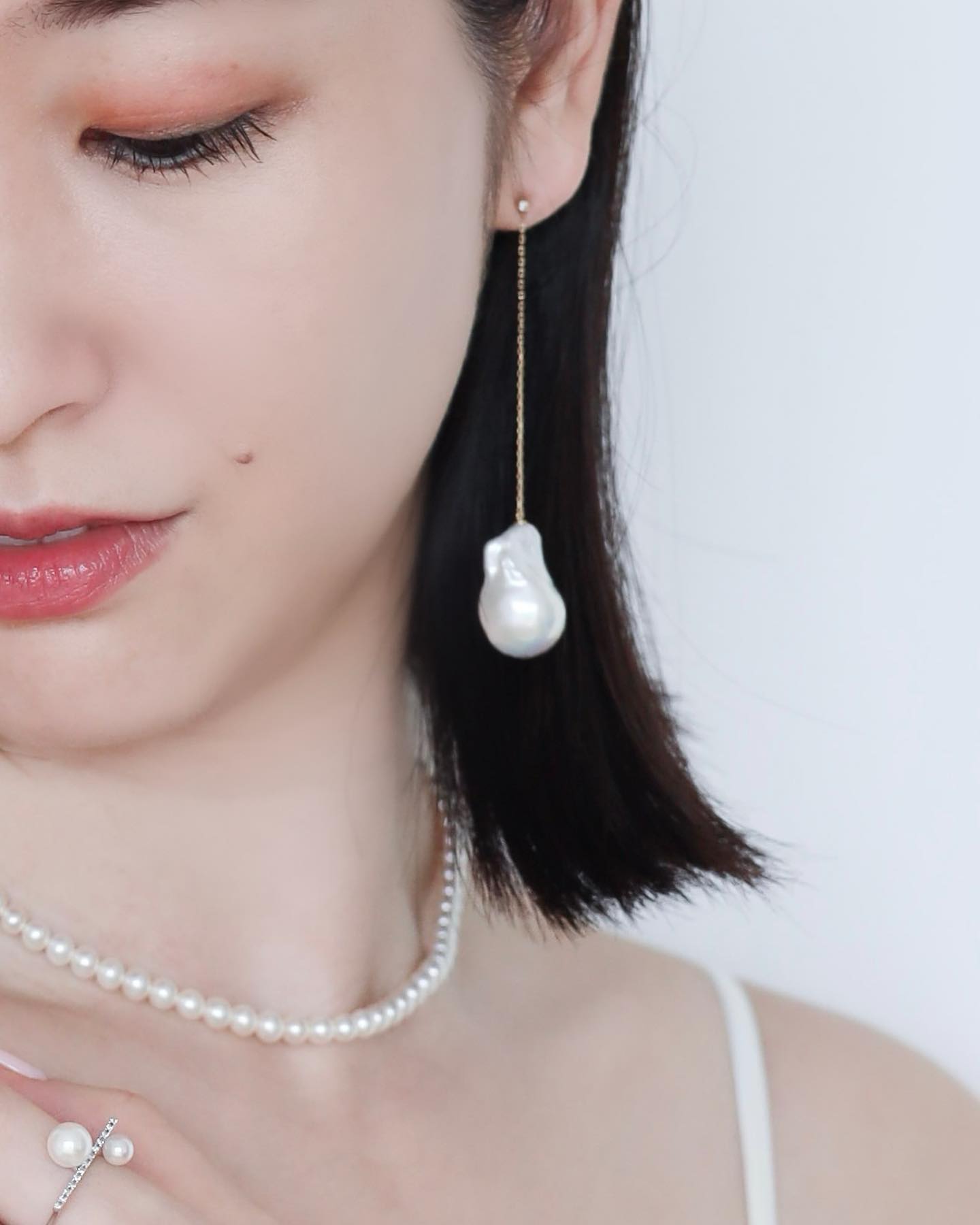 Half-faced asian woman wearing Baroque Pearl Swing Earrings paired with Akoya Baby Pearl Classic Necklace and Akoya Diamond Bar Ring on left index finger
