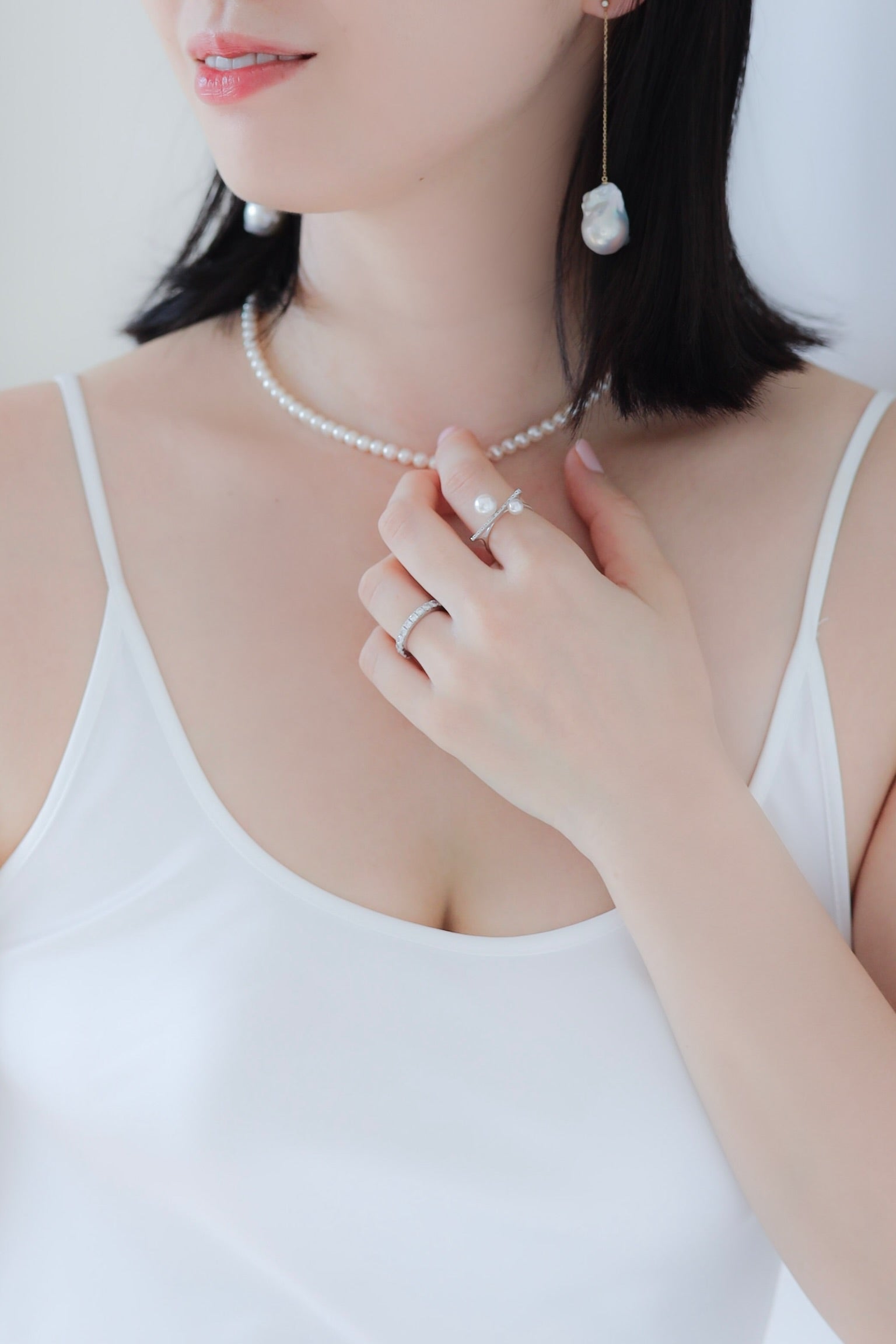 Woman wearing Baroque Pearl Swing Earrings paired with Akoya Baby Pearl Classic Necklace and Akoya Diamond Bar Ring on left index finger