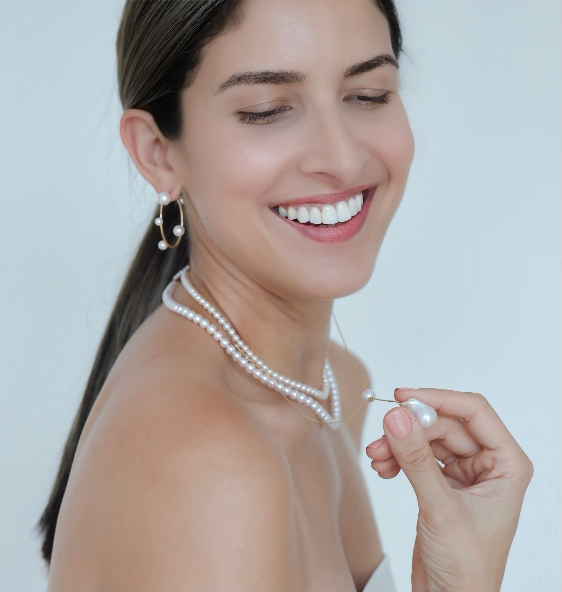 Woman wearing Akoya Hoop Earrings paired with 2 Akoya Baby Pearl Classic Necklace with a Baroque Pearl Charm hooked onto one of the 2 necklace