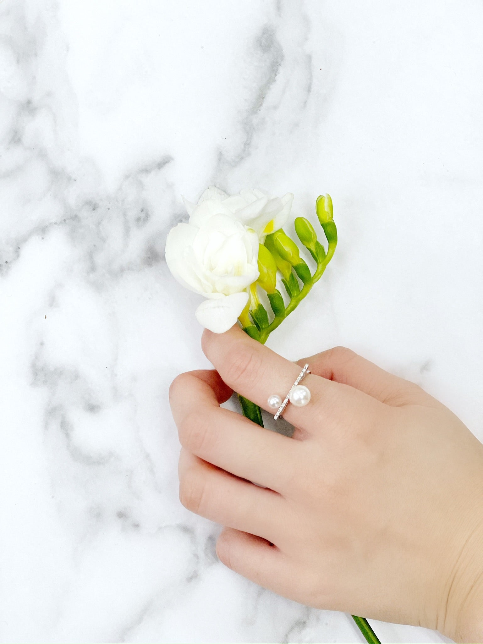 Closeup of Akoya Diamond Bar Ring on finger with marble background and a plant